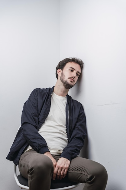 Photo gratuite jeune homme espagnol déprimé assis sur une chaise, la tête appuyée contre un mur