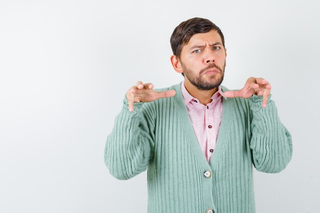 Jeune homme essayant d'effrayer quelqu'un en chemise, cardigan et semblant sérieux, vue de face.