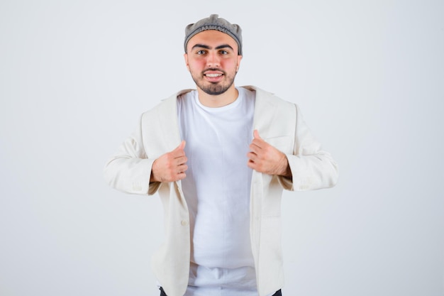 Jeune homme essayant d'enlever la veste et posant à l'avant en t-shirt blanc, veste et casquette grise et l'air heureux