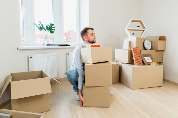 Jeune homme essayant de porter la pile de cartons à la maison