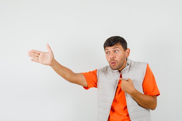 Jeune homme étendant la main tout en se montrant en t-shirt, veste et à la perplexité. vue de face.