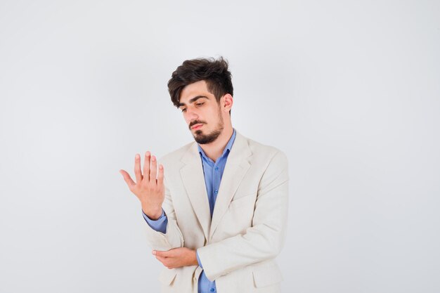 Jeune homme étirant les mains comme tenant quelque chose et le regardant en chemise bleue et veste de costume blanche et à l'air concentré