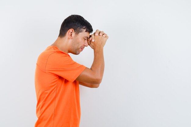 Jeune homme étreignant les mains en geste de prière en t-shirt orange et à la recherche d'espoir.