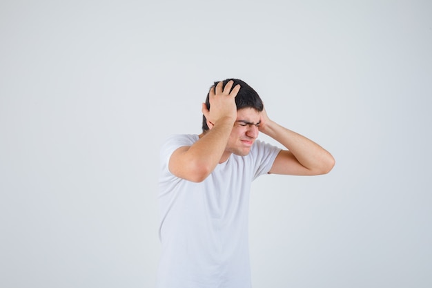 Jeune homme étreignant la tête avec les mains en t-shirt et l'air stressé. vue de face.