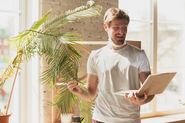 Jeune homme étudiant à la maison lors de cours en ligne pour jardinier, biologiste, fleuriste. Obtenir une profession tout en étant isolé, mettre en quarantaine contre la propagation du coronavirus. Utilisation d'un ordinateur portable, d'un smartphone, d'un casque.