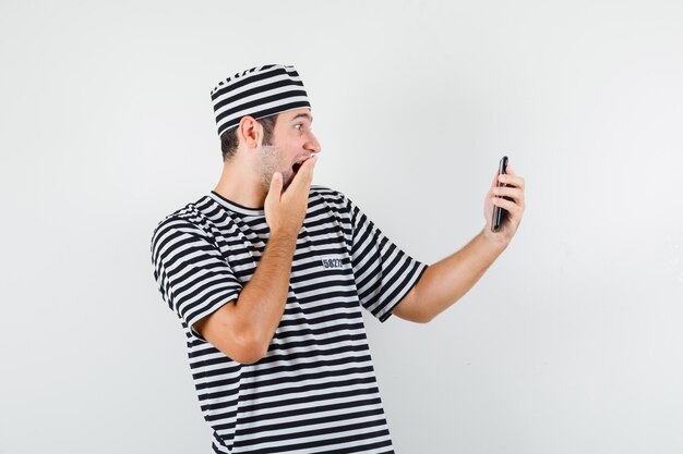 Jeune homme faisant un appel vidéo en t-shirt, chapeau et à la vue étonné, de face.