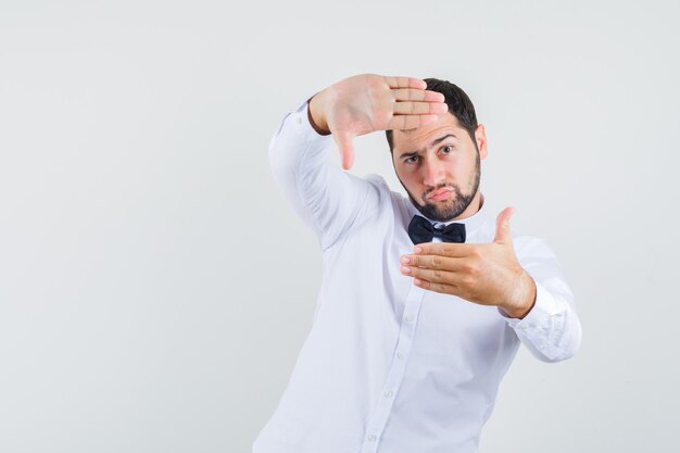 Jeune homme faisant le geste du cadre en chemise blanche et à la vue de face, focalisée.