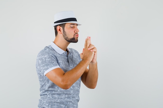 Jeune Homme Faisant Le Geste Du Pistolet De Tir En T-shirt Rayé, Chapeau Et à La Recherche Concentrée. Vue De Face.