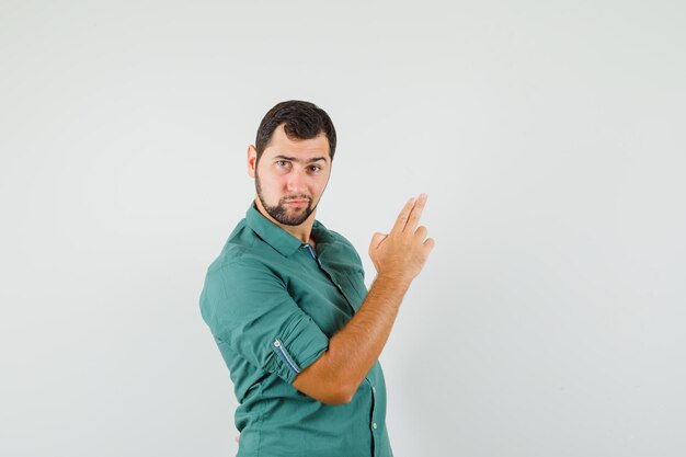 Jeune homme faisant un geste de pistolet en chemise verte et ayant l'air sérieux. vue de face.