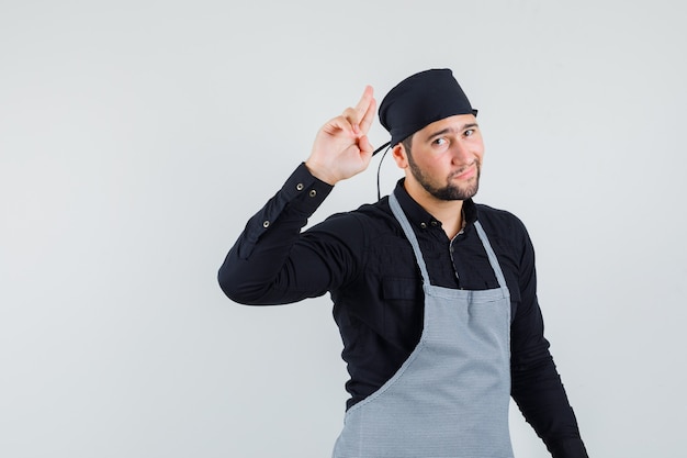 Jeune Homme Faisant Des Gestes Avec Deux Doigts En L'air En Chemise, Tablier Et à La Cool, Vue De Face.