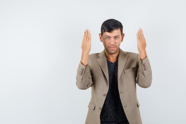 Jeune homme faisant des gestes avec les mains levées en t-shirt, veste et à la joyeuse vue de face.