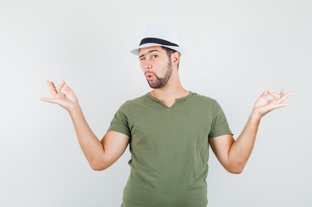 Jeune homme faisant la méditation et clignant des yeux en t-shirt vert et chapeau