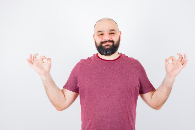 Jeune homme faisant de la méditation en t-shirt rose et ayant l'air concentré. vue de face.