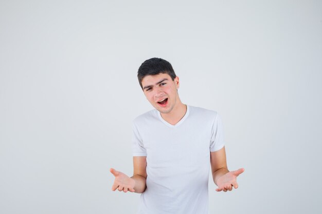 Jeune homme faisant semblant de montrer quelque chose en t-shirt et à la joyeuse vue de face.