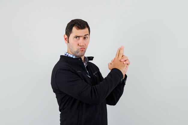 Jeune homme faisant signe de pistolet à doigt en chemise, veste et à la confiance