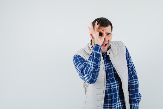 Jeune homme faisant le tour sur son œil en chemise, veste sans manches et à la recherche amusée. vue de face. espace pour le texte