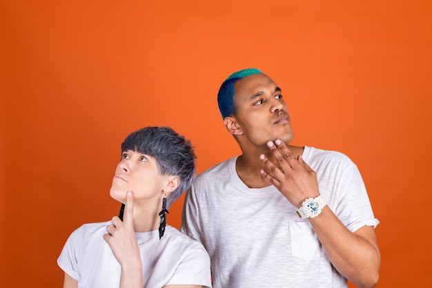Jeune homme et femme en blanc décontracté sur un mur orange regard pensif de côté tenant le menton