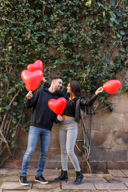 Jeune homme et femme souriante tenant des ballons en forme de coeurs