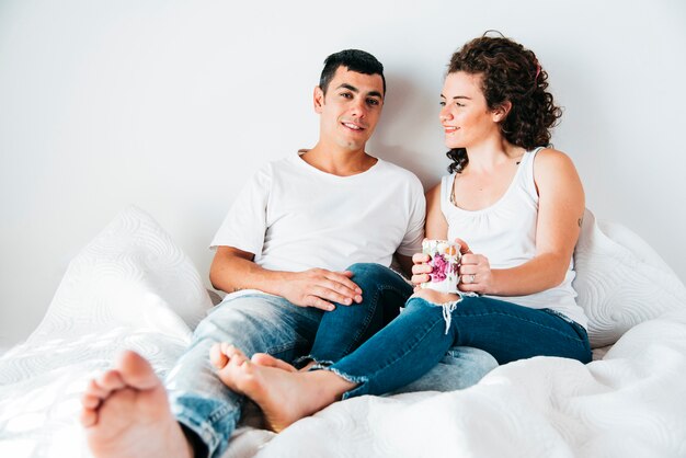 Jeune homme et femme avec tasse assis sur le lit