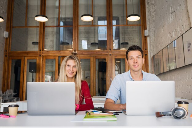 Jeune homme et femme travaillant sur un ordinateur portable dans un espace ouvert, bureau de travail collaboratif