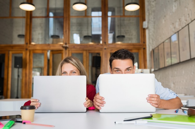 Jeune homme et femme travaillant sur un ordinateur portable dans un espace ouvert, bureau de travail collaboratif