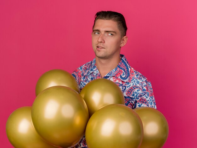 Jeune homme de fête arbitré vêtu d'une chemise colorée debout derrière des ballons isolés sur rose