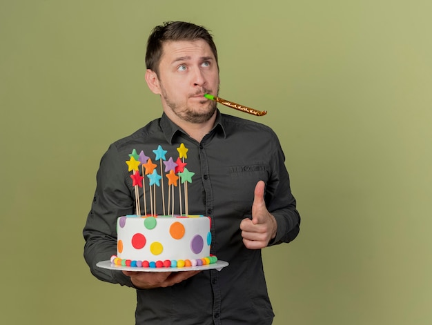 Jeune homme de fête portant une chemise noire et un chapeau bleu tenant un gâteau soufflant sifflet vous montrant geste isolé sur vert olive