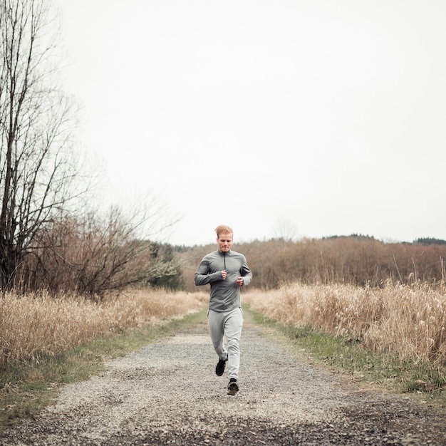 Jeune homme fitness en cours d&#39;exécution sur un chemin de terre sur le terrain