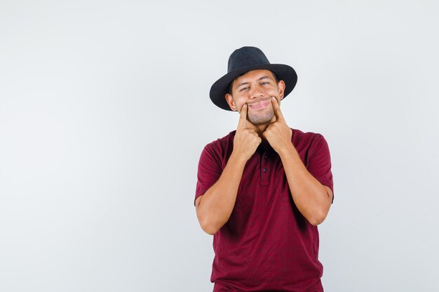 Jeune homme forçant un sourire sur le visage en t-shirt, vue de face de chapeau.