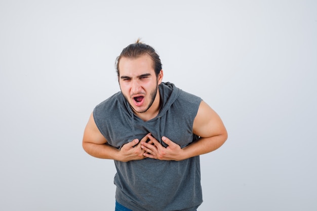 Jeune homme en forme se sentant nauséeux en sweat à capuche sans manches et à la recherche de mal, vue de face.