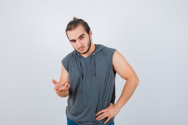 Jeune homme en forme de sweat à capuche sans manches étirant la main vers la caméra et à la recherche pensive, vue de face.