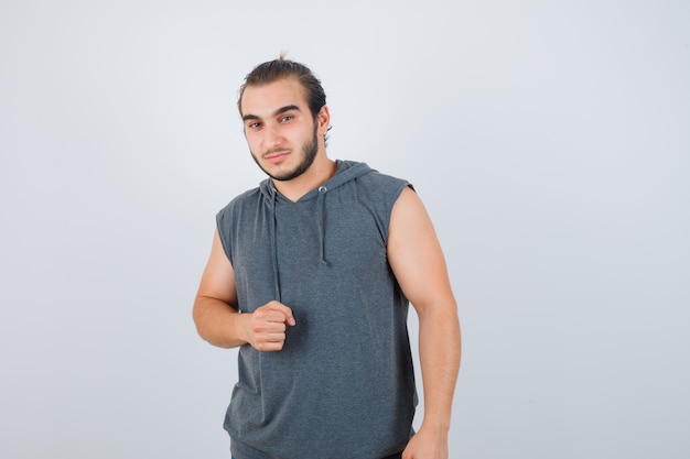 Jeune homme en forme en sweat à capuche sans manches montrant le poing fermé et à la vue de face, confiant.