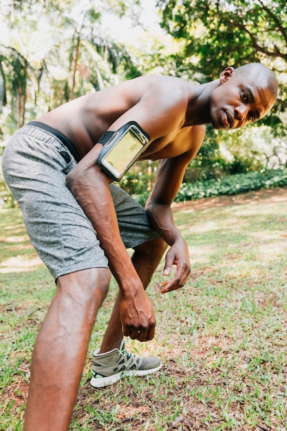 Jeune homme en forme de torse nu avec téléphone portable dans l&#39;étui à brassard qui s&#39;étend de la jambe