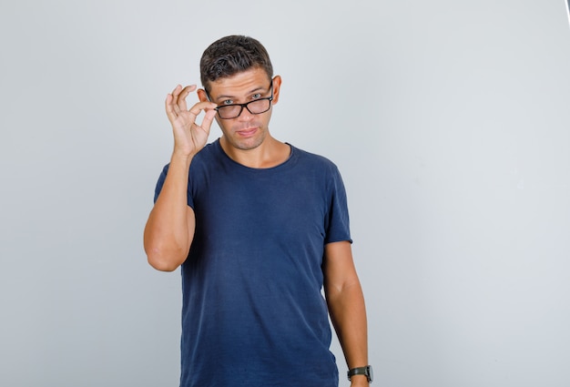 Jeune homme furtivement par-dessus des lunettes en t-shirt bleu foncé, vue de face.