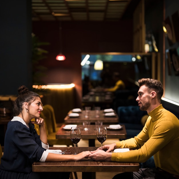 Jeune homme, gai, femme, tenant mains, table, à, verres vin, dans restaurant