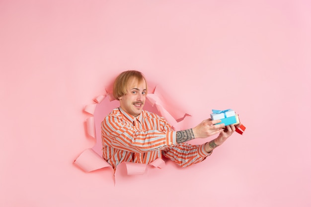 Un jeune homme gai pose dans un mur de trou de papier de corail déchiré émotionnel et expressif