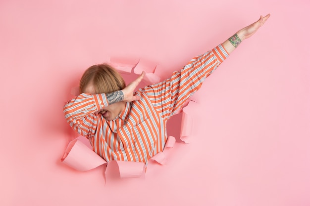 Un jeune homme gai pose dans un mur de trou de papier de corail déchiré émotionnel et expressif