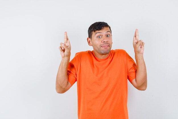 Jeune homme en gardant les doigts croisés en t-shirt orange et à l'optimiste