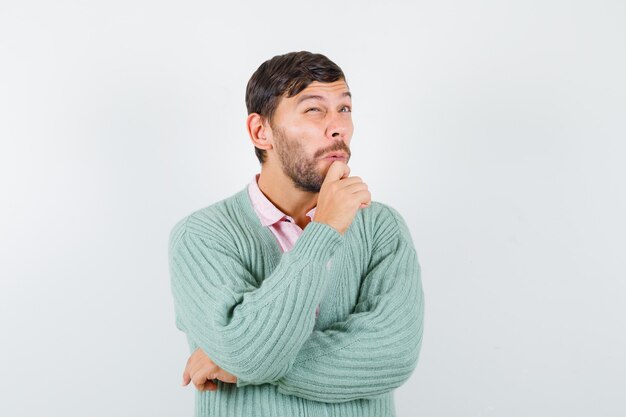 Jeune homme gardant la main sur le menton, levant la chemise, le cardigan et l'air réfléchi, vue de face.