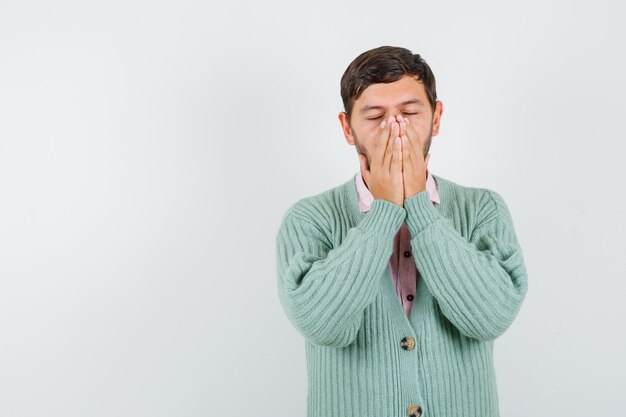 Jeune homme gardant les mains sur le visage tout en fermant les yeux en chemise, cardigan et ayant l'air épuisé. vue de face.