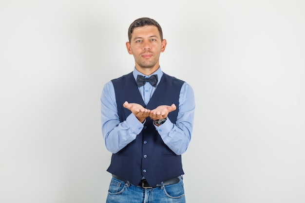 Jeune homme gardant les paumes ouvertes ensemble en costume, jeans et à la gaieté.