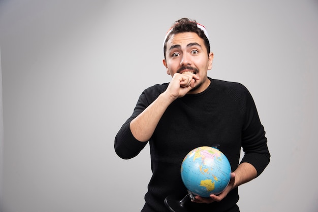 Jeune homme avec globe dans le chapeau du père Noël se mordant le poing.