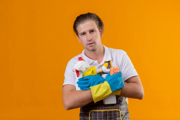 Jeune homme hansdome portant un tablier et des gants en caoutchouc tenant des outils de nettoyage