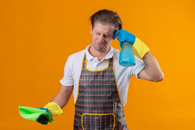 Jeune homme hansdome portant un tablier et des gants en caoutchouc tenant un spray de nettoyage et un tapis