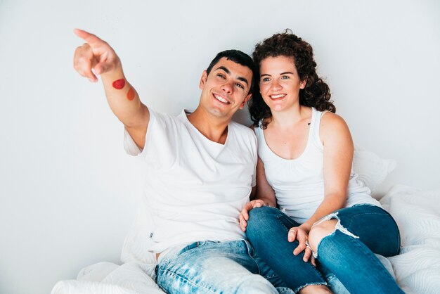 Jeune homme heureux avec la main tendue et femme assise sur le lit
