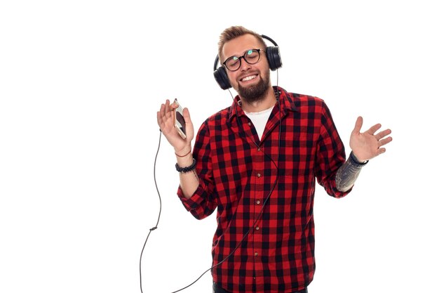 Jeune homme hipster en chemise à carreaux et lunettes portant des écouteurs à la recherche de plaisir sur fond blanc. Tourné en studio. Copier l'espace