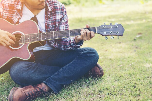Jeune homme hipster pratiqué la guitare dans le parc, heureux et profiter de p