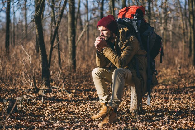 Jeune homme hipster voyageant avec sac à dos dans la forêt d'automne portant une veste chaude et un chapeau, touriste actif, explorant la nature en saison froide