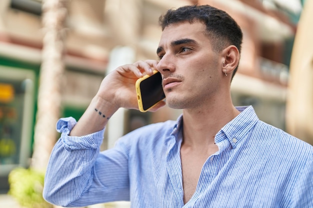Jeune homme hispanique parlant sur le smartphone avec une expression sérieuse dans la rue