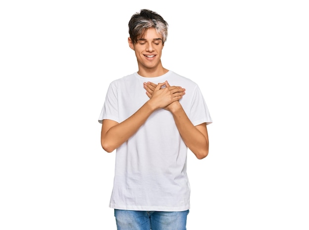 Photo gratuite jeune homme hispanique portant un t-shirt blanc décontracté souriant avec les mains sur la poitrine avec les yeux fermés et un geste reconnaissant sur le concept de santé du visage